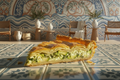 Kolokithopita on a white and blue tile by a sunlit window by the sea
